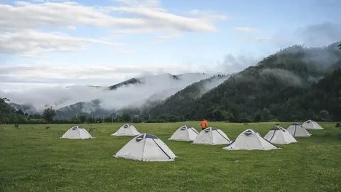 山间云雾下，草地上分布着营员的露营帐篷