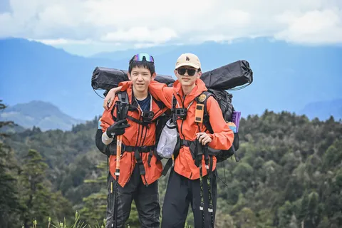 两名远征营员背着重装背包，在山野中搭肩合影