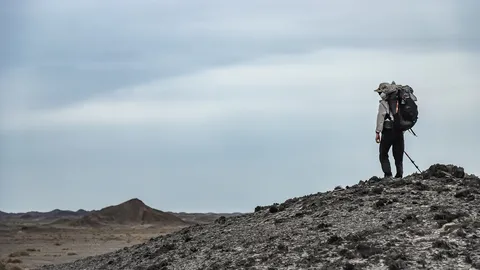 背负重装背包的营员站在戈壁山坡上，手持登山杖眺望前方