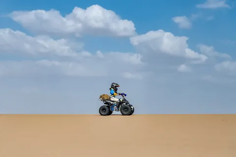 沙漠 ATV 营员戴着头盔驾驶四轮车行过沙丘